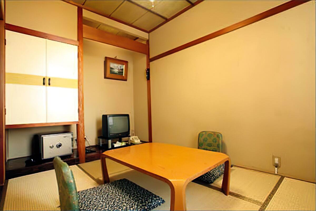 Quarto japonês tradicional com tatames, uma mesa de madeira baixa, televisão e uma cadeira verde.
