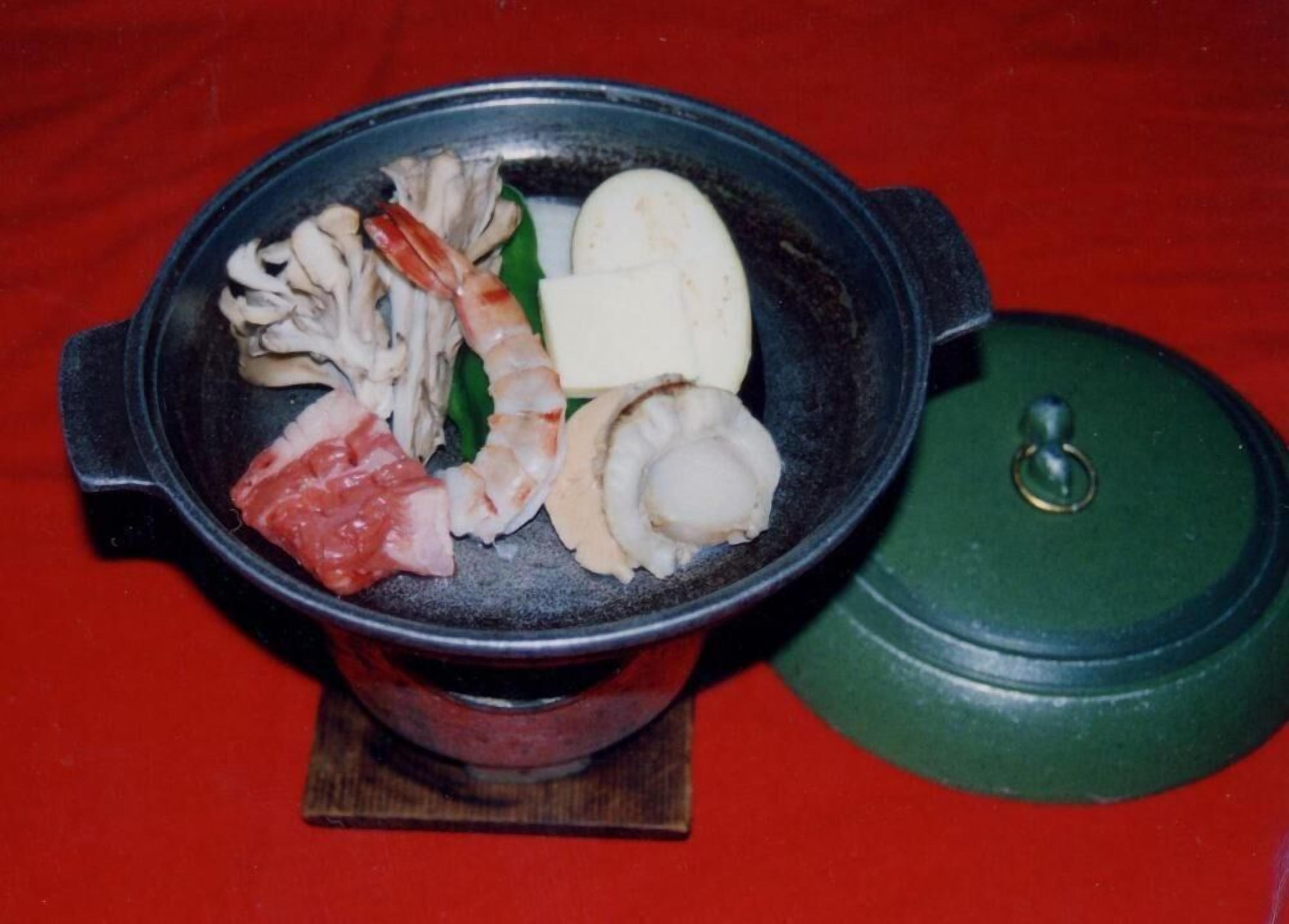 A hot pot with various meats and seafood, including shrimp and scallops, on a red table.