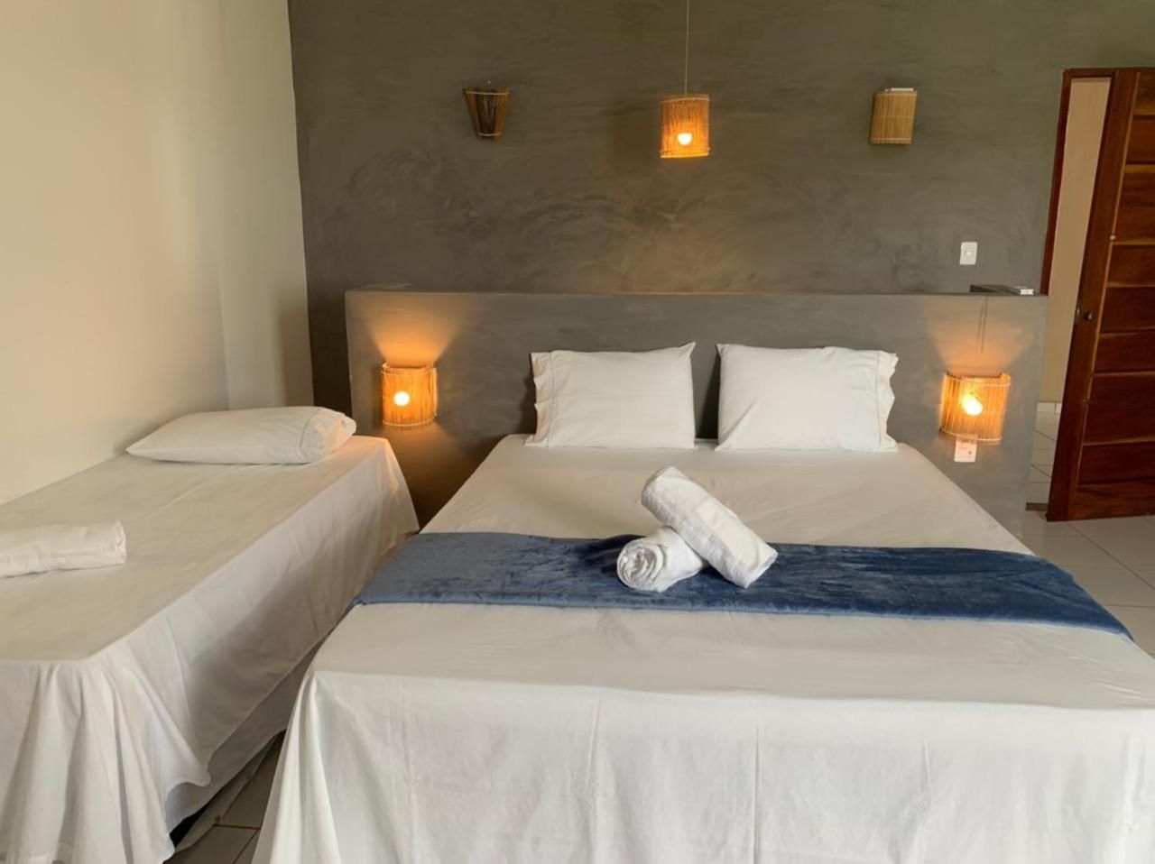 Ein Hotelzimmer mit zwei Einzelbetten, einem großen Bett mit blauer Decke und Wandlampen.