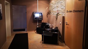 A reception area with a reception desk, a mounted television, a wall-mounted plant, and a door labeled "Zu den Zimmern". - greenpartment Boardinghouse Hotel Ingolstadt Friedrichshofen (Ingolstadt)