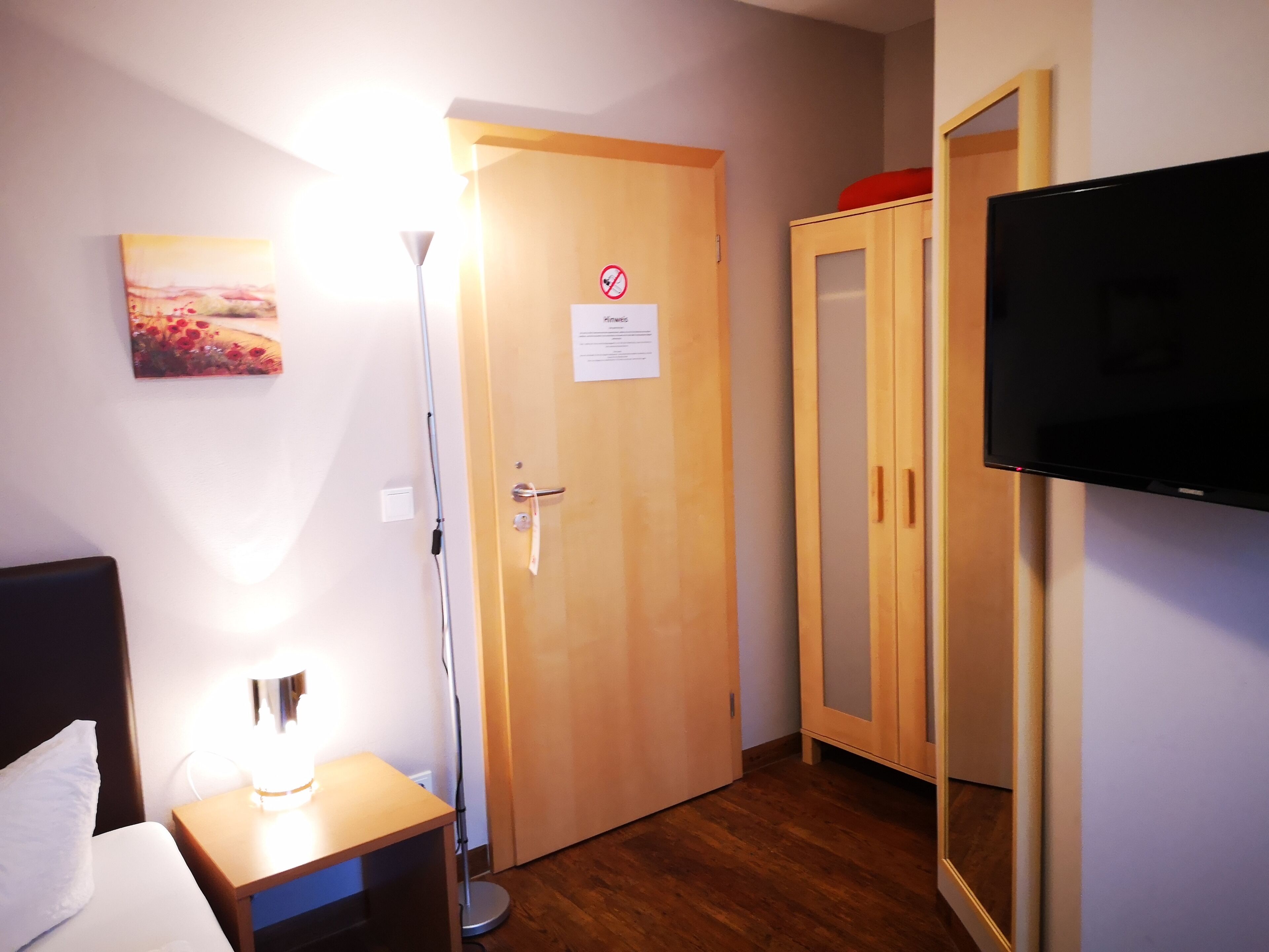 A hotel room with a bed, bedside lamp, wooden wardrobe, and a television.