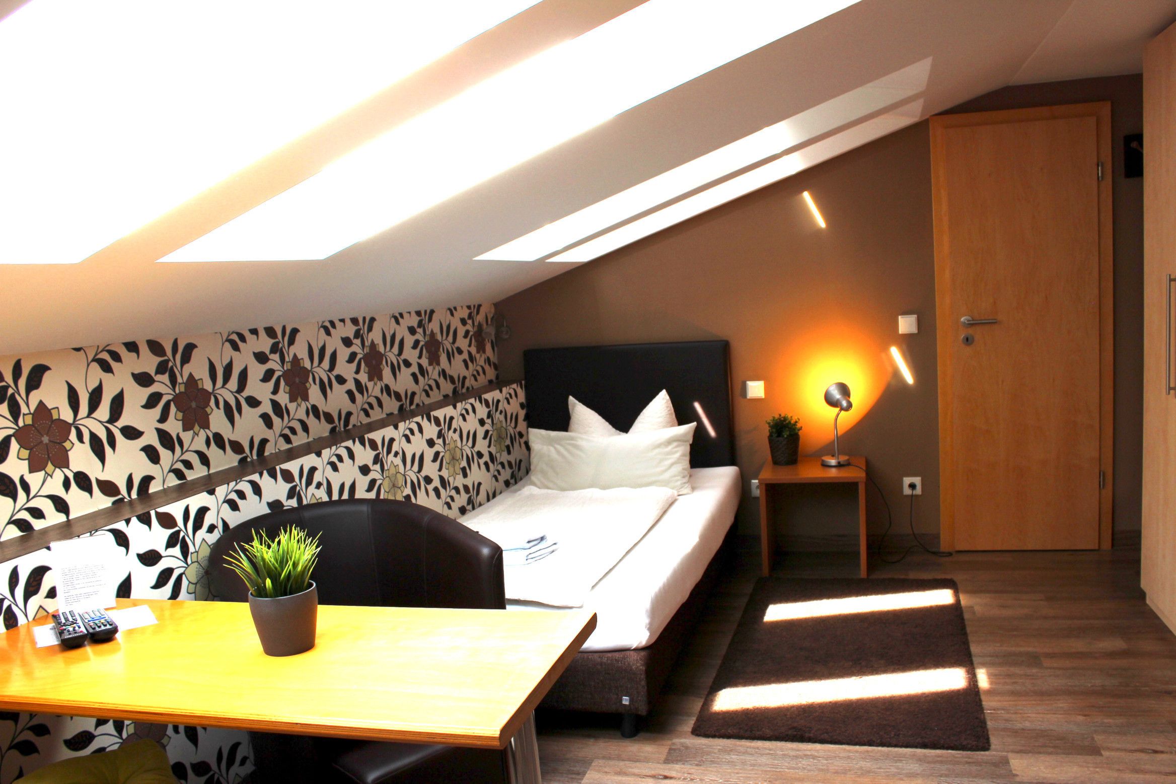 Une chambre à coucher comprenant un lit, un bureau, une chaise, une plante en pot et une table de chevet avec une lampe.