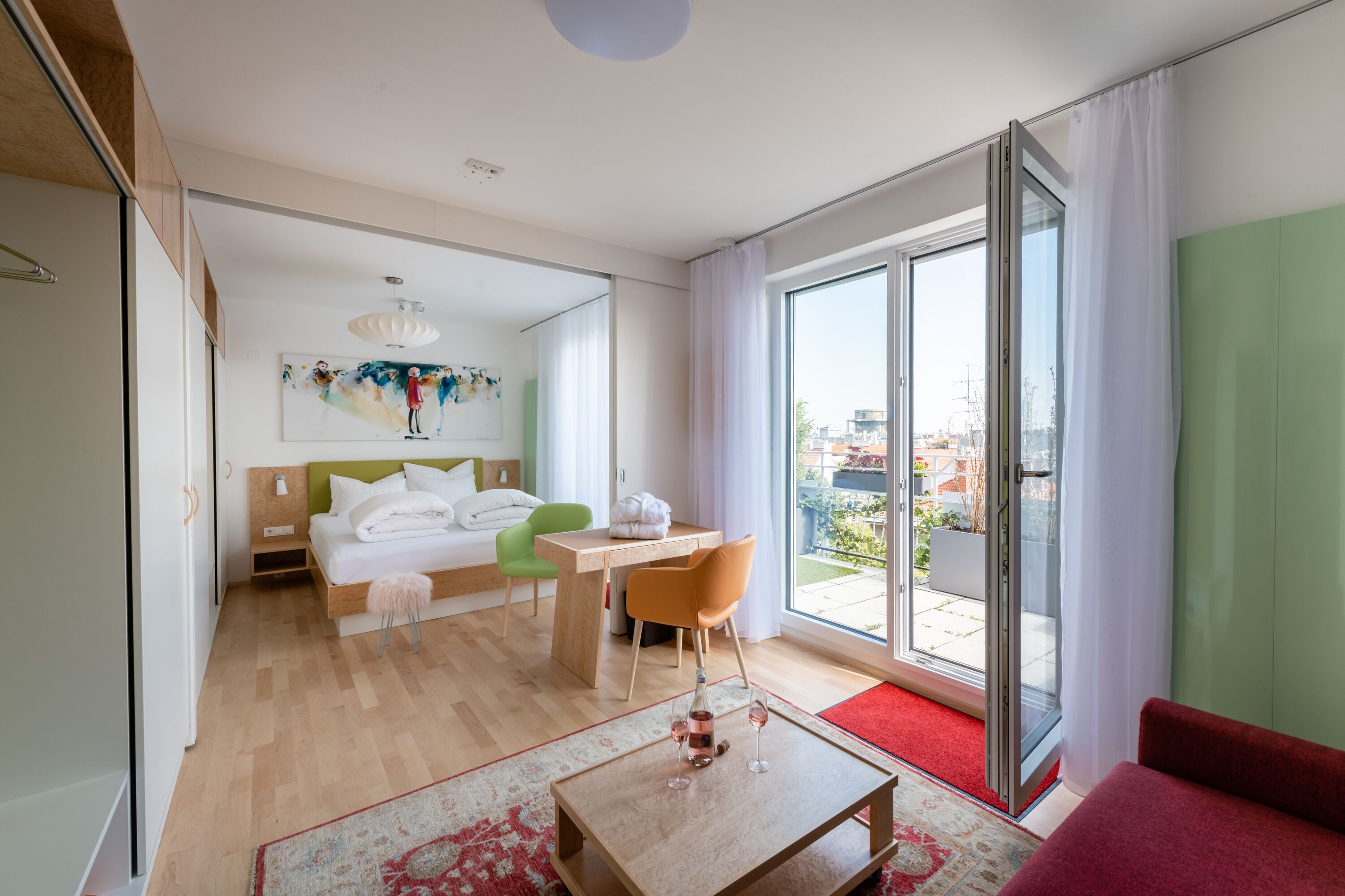 Ein modernes Hotelzimmer mit einem Bett, einem Schreibtisch, einem Stuhl, einem Couchtisch und einer großen Schiebeglasdoor zum Außenbereich.