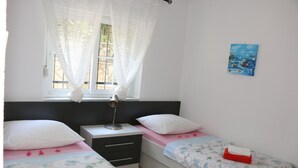 A bedroom with two single beds, a nightstand, a lamp, a window with sheer curtains, and a painting on the wall. - Villa Mara (Slivno)