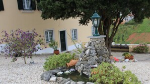 Un jardin avec un bassin, des rochers et des plantes en pot.