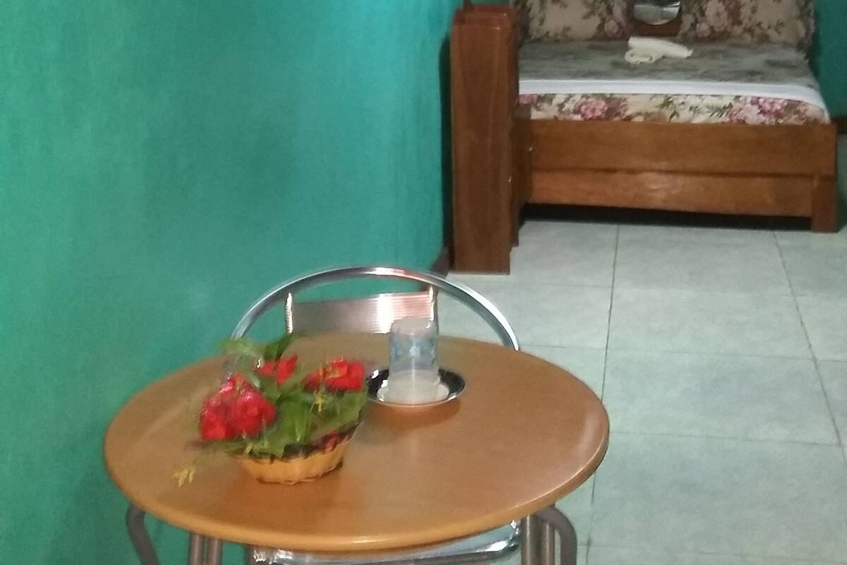 A small room with teal walls, a wooden sofa with floral upholstery, and a metal-framed table with a bowl of fruit.