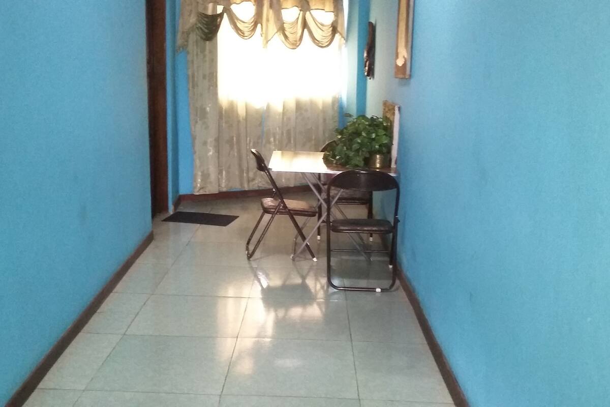 A narrow hallway with blue walls and a tiled floor leading to a dining area with a table and chairs.