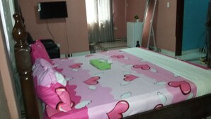 Un dormitorio con una cama cubierta con ropa de cama estampada en rosa y blanco, un cabecero de madera, una mesita de noche y un espejo en la pared.