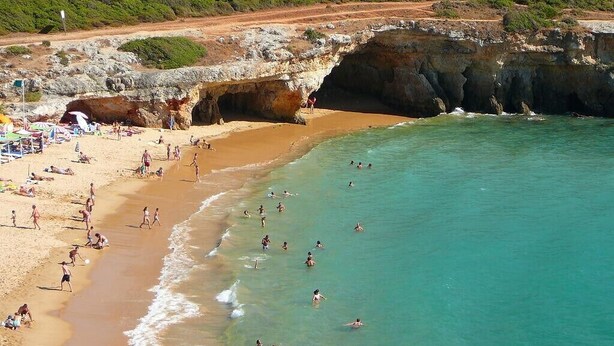 A beach with people swimming and sunbathing, a rocky cliff, and a dirt path leading up to the beach. - Sun terrace with beautiful sea views, 4 beautiful beaches, quiet location (Ferragudo)