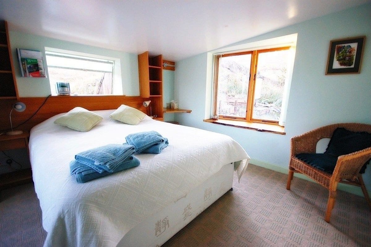 Un dormitorio con cama, una silla, un ventanal y una estantería.