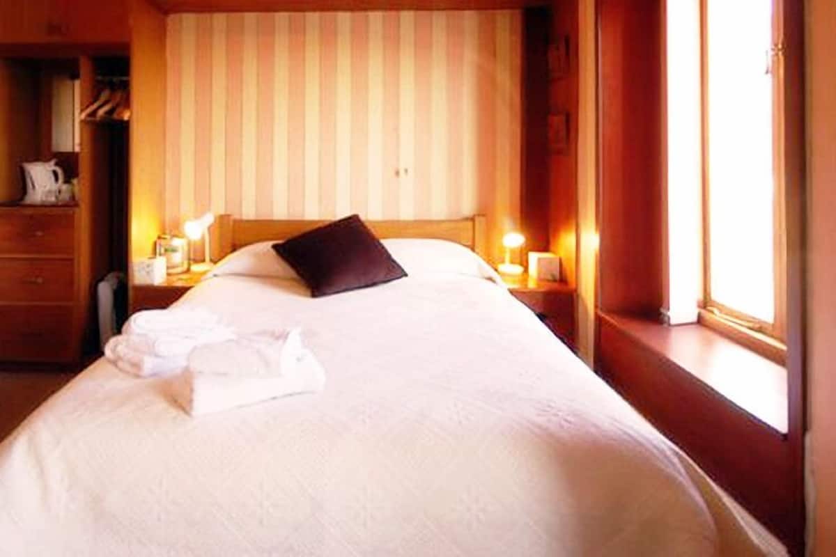 Habitación de hotel con una cama grande, una mesita de noche con lámpara, una ventana con cortinas y un armario de madera.