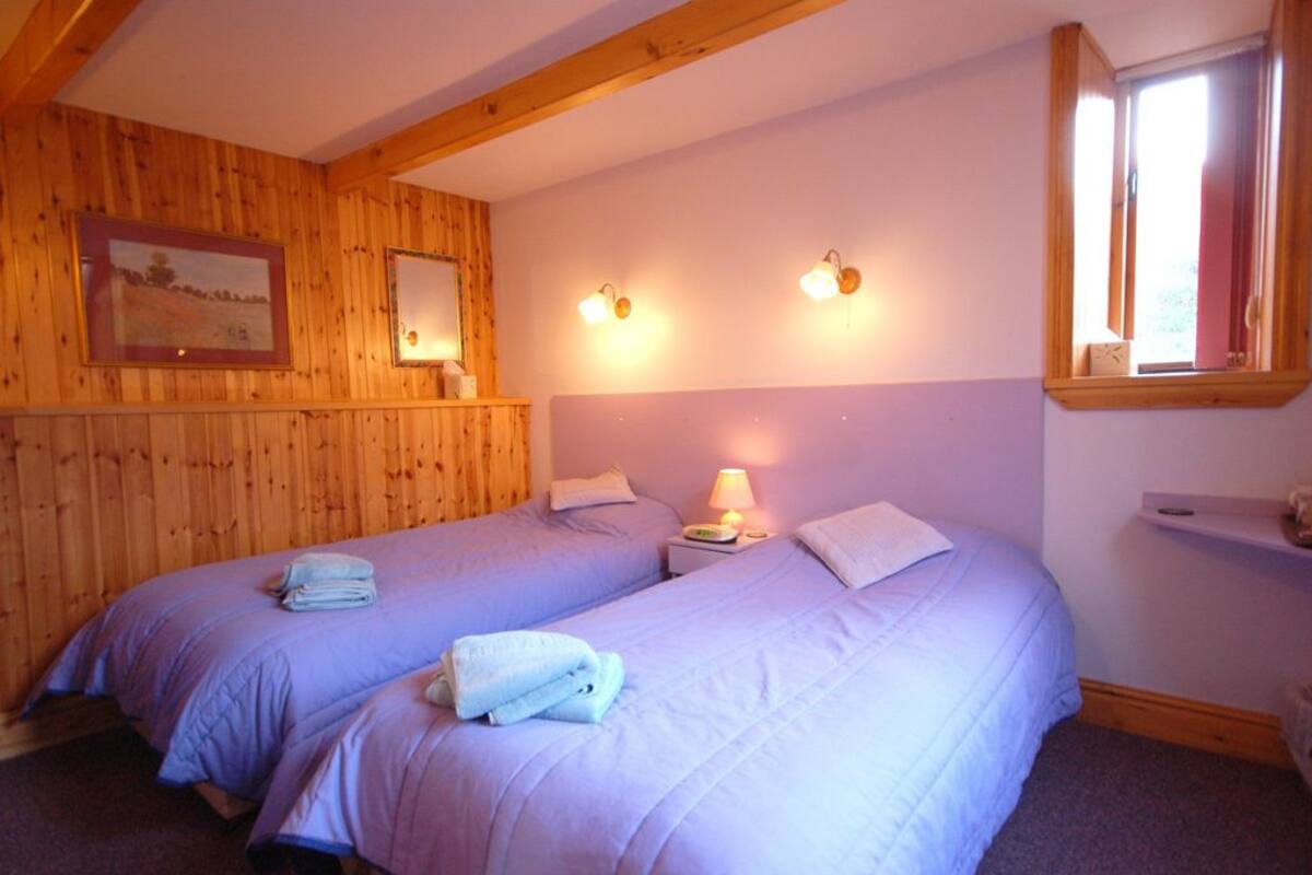 Una habitación con dos camas, paredes de madera, un ventanal y luces fijadas a la pared.