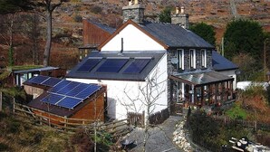 Ein Haus mit weißer Fassade, einem Steinsschornstein und Solaranlage auf dem Dach.
