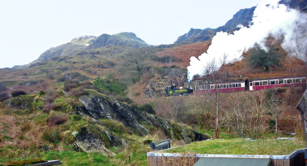 Um trem a vapor com vagões de passageiros atravessando uma paisagem montanhosa.