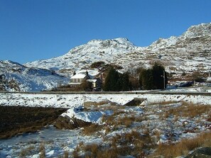 Uma casa com paisagem coberta de neve e montanhas ao fundo.