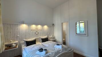 A bedroom with a bed, bedside tables, a chandelier, a wall-mounted shelf, and a window.