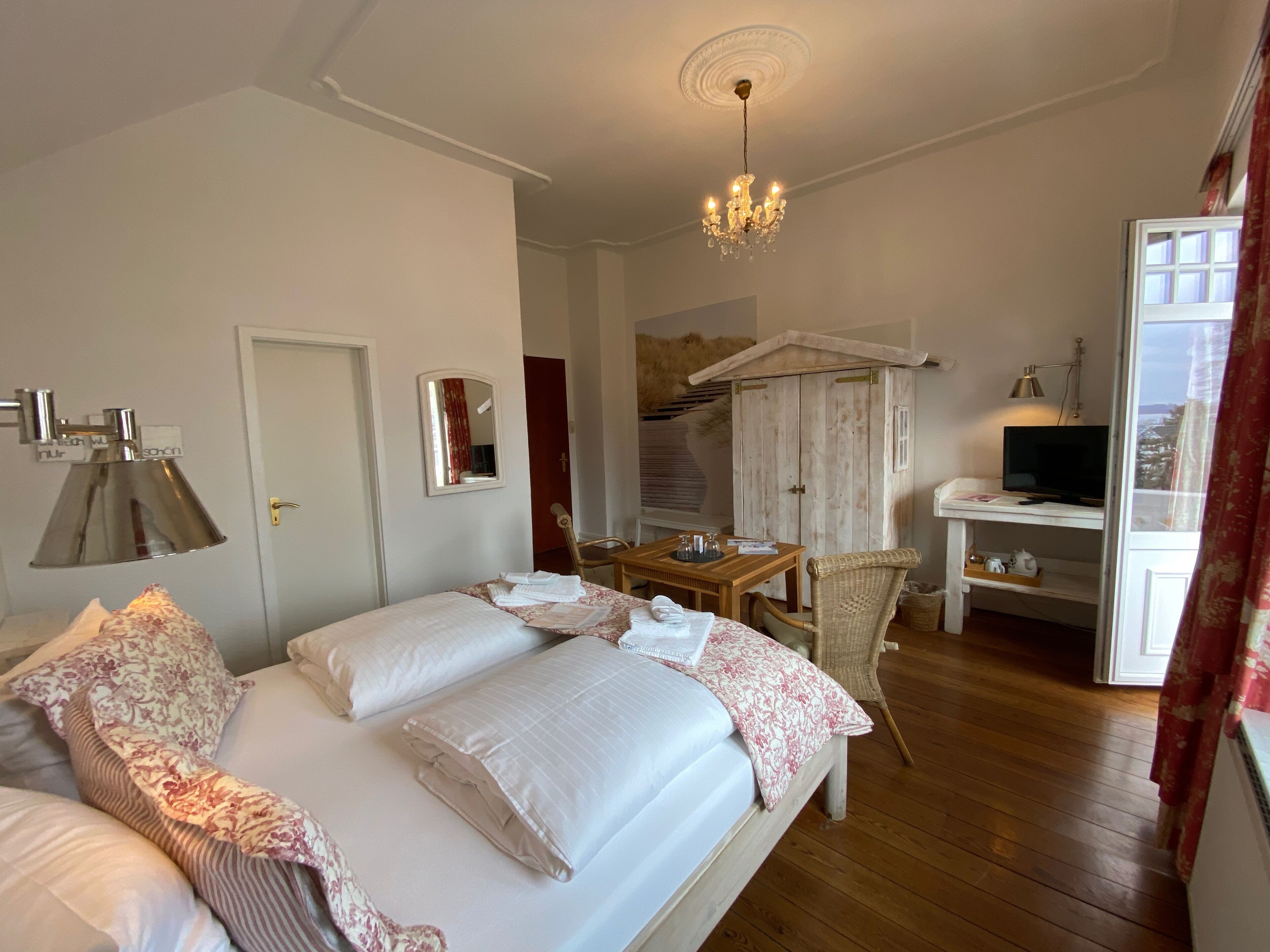 A bedroom with a bed, bedside table, lamp, wardrobe, TV, and a view of the outside.