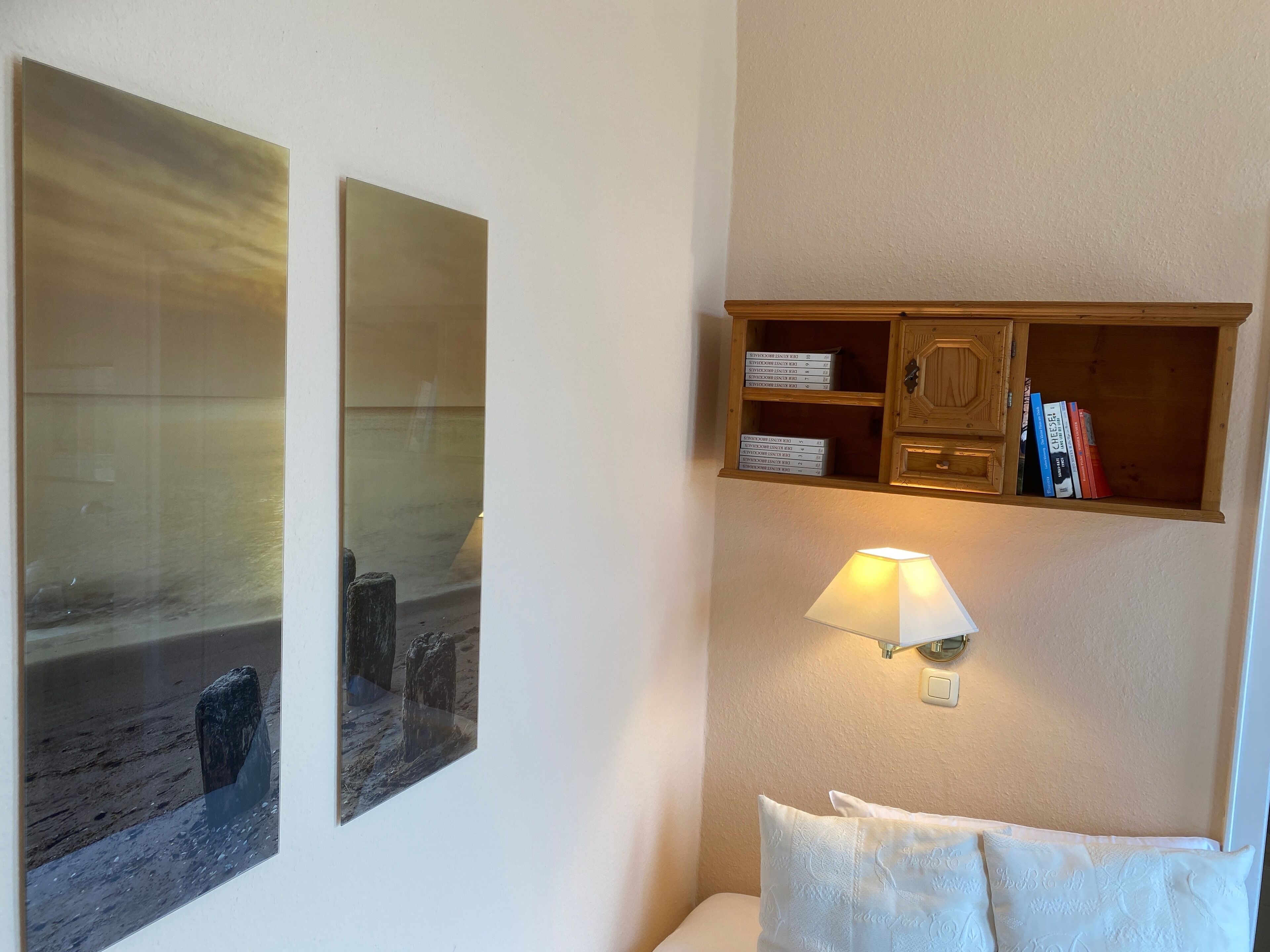 Una habitación con una cama, un estante con libros y dos cuadros enmarcados.