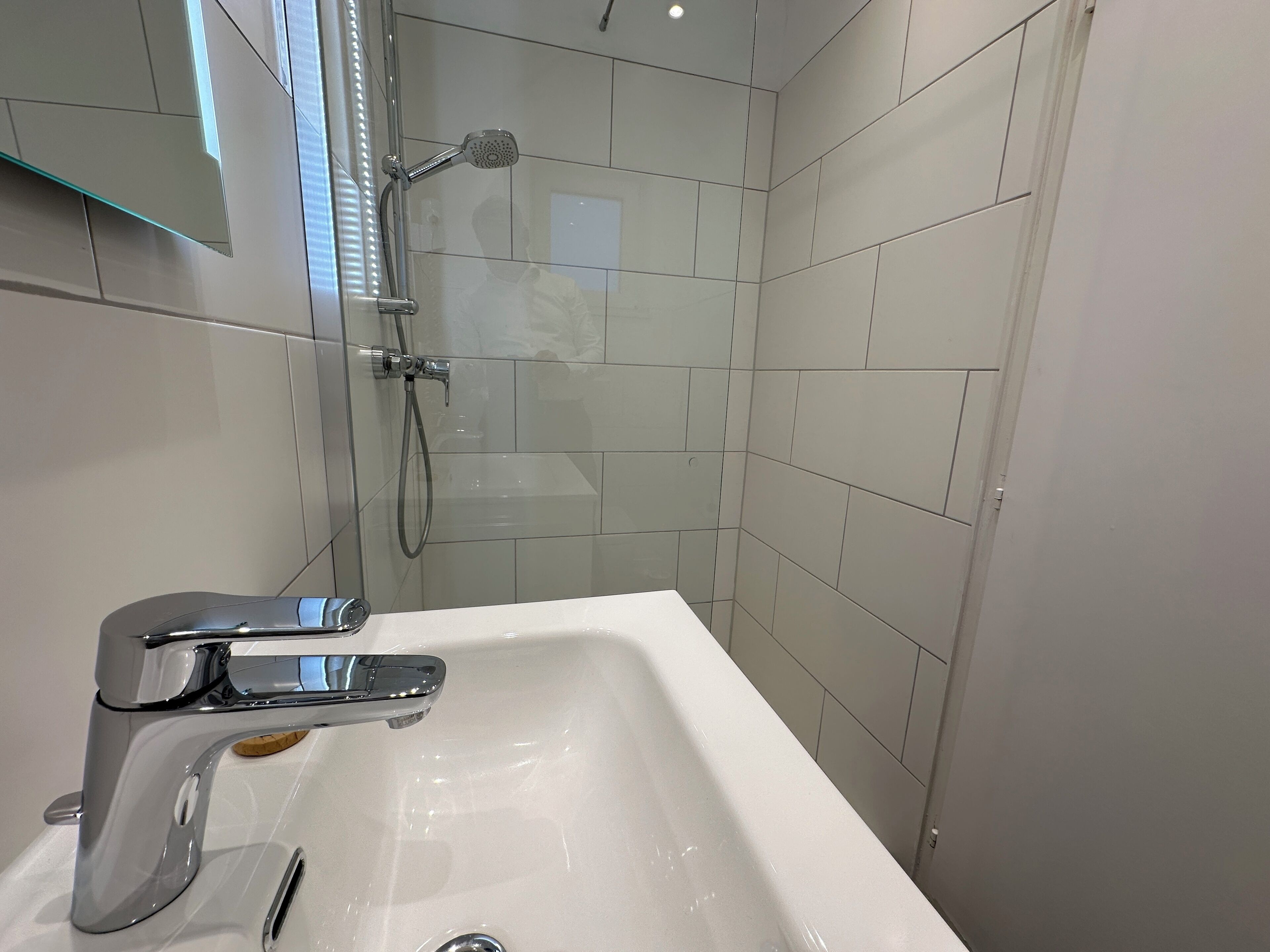 Un baño moderno con un lavamanos blanco, grifo cromado y cabezal de ducha de mano.