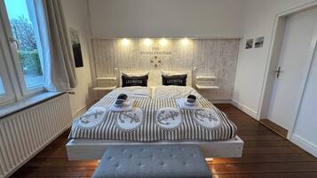 A double bed with striped bedding, two pillows with 'LEXINGTON' text, a bedside table, a bench, and a view of the outside through a window.