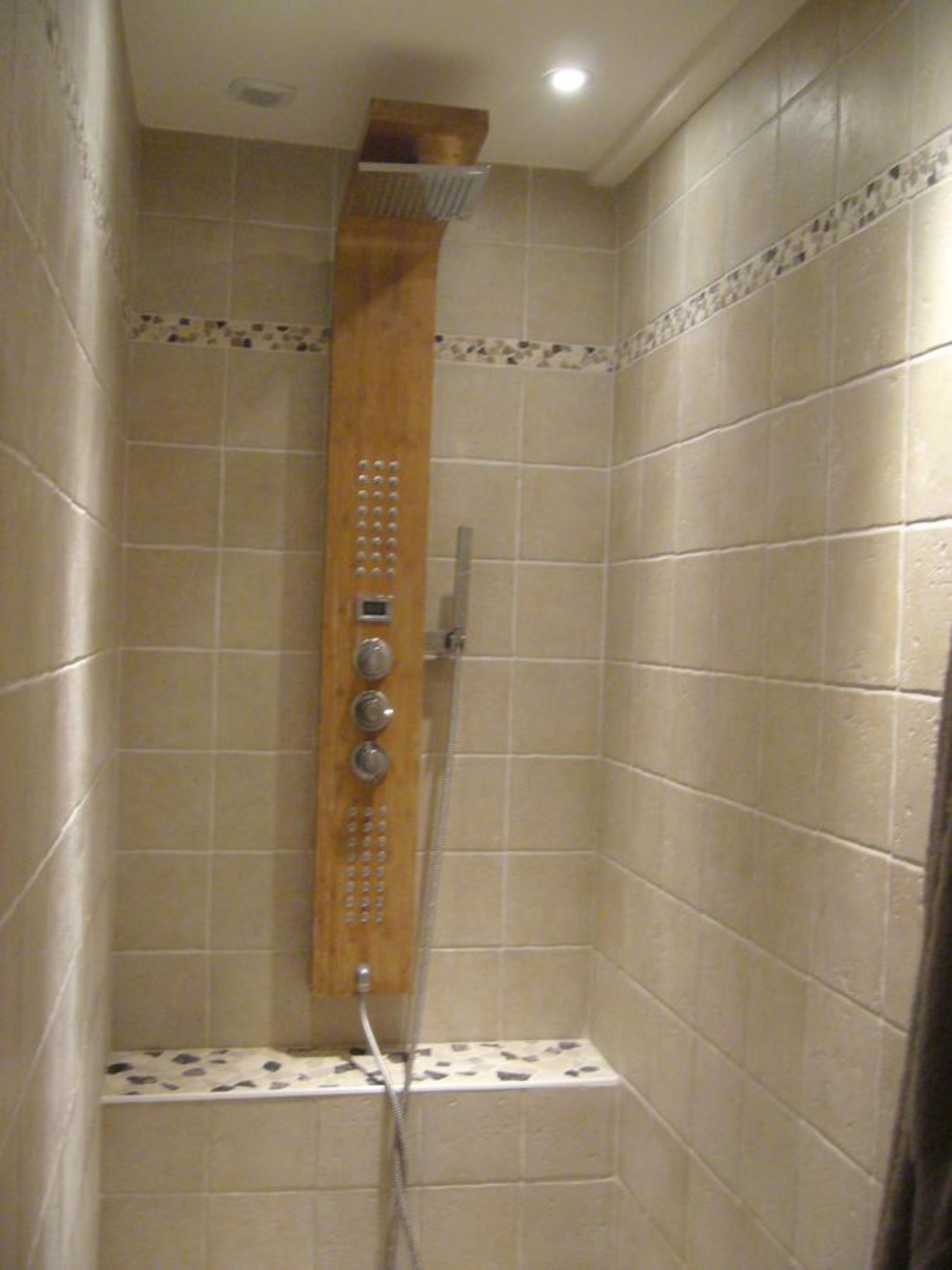 A shower with a wooden panel, a handheld showerhead, and a control panel.