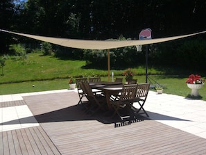 Une terrasse extérieure avec une table et des chaises en bois, entourée de plantes en pot et d’un panier de basketball.