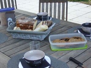 Une table en bois avec un panier de pain, un récipient rempli de biscuits, un bol et une tasse.