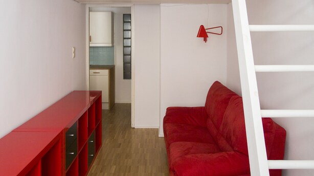 Quarto compacto com beliche, sofá vermelho, estante vermelha e escada branca.
