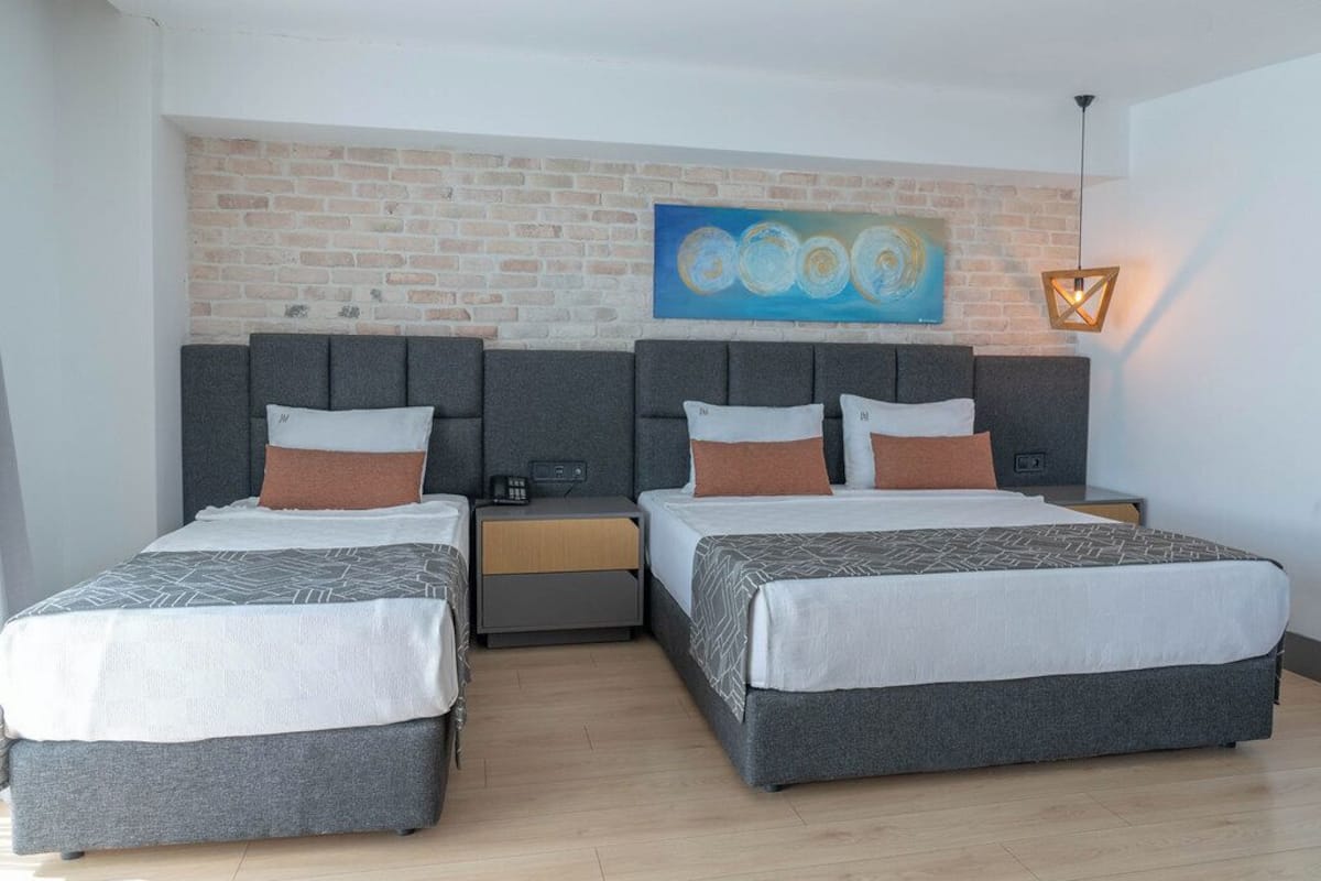 A double room with two beds, a brick wall, a painting, and a nightstand with a lamp.