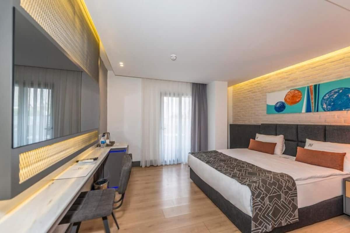 A modern hotel room with a large bed, a desk, a chair, and a large mirror.