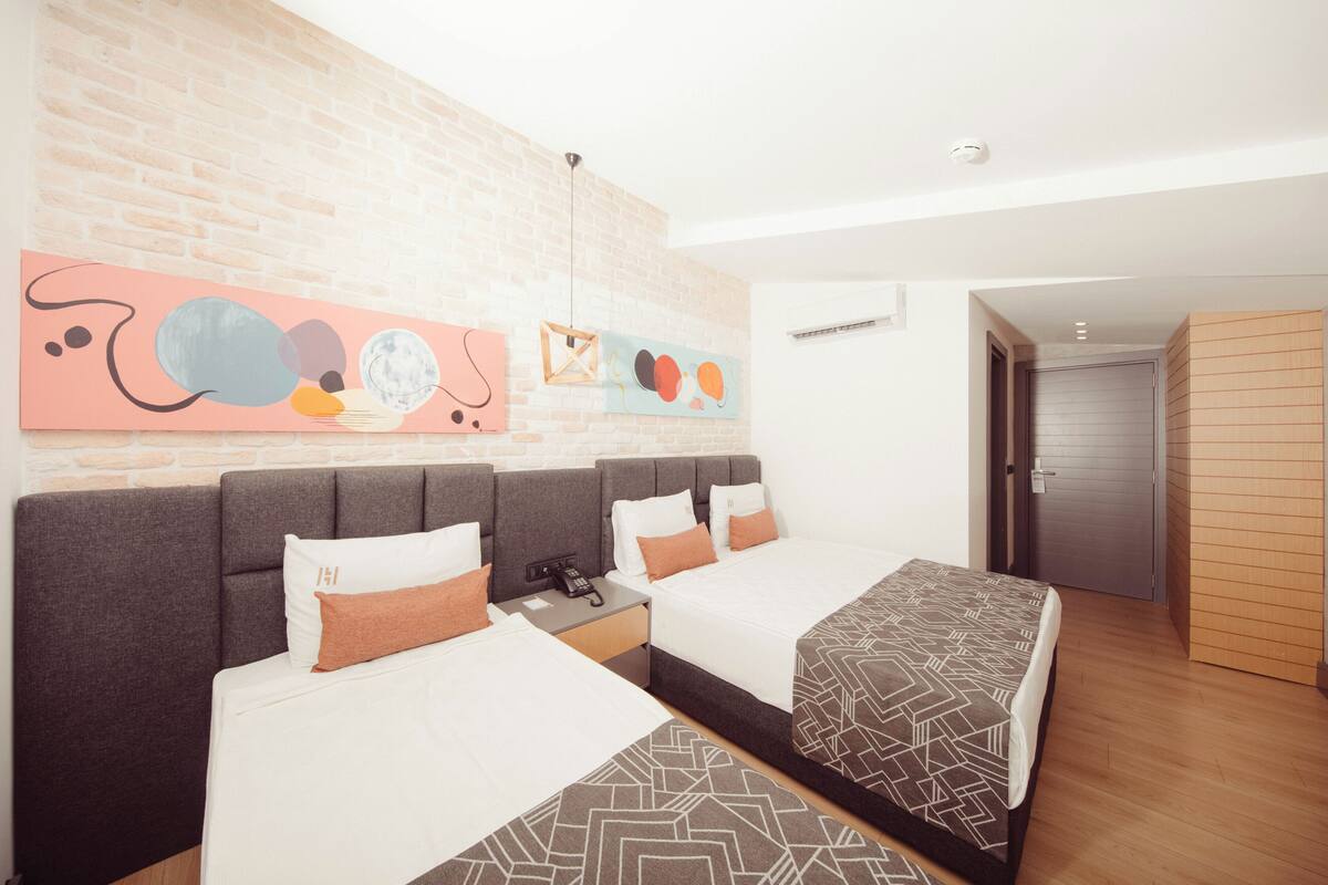 A hotel room with two beds, a brick wall, abstract art, and a wooden door.