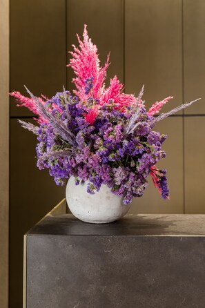 A white vase with a floral arrangement on a dark, rectangular surface. - Hotel Scenario (Rome)