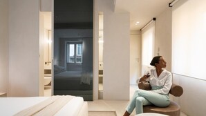 A modern hotel room with a bed, a sitting area with a table, and a large mirror. - Hotel Scenario (Rome)