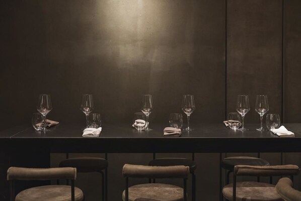 A dark dining table with six wine glasses and folded napkins, flanked by four chairs.