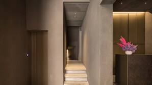 A modern interior with a staircase leading to an elevator, a reception desk with a decorative plant, and a minimalist design. - Hotel Scenario (Rome)