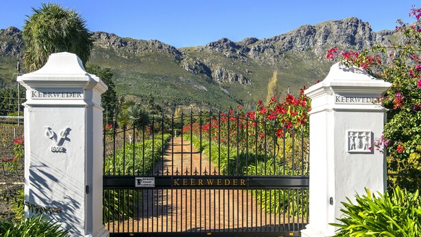 A gated entrance with the name 'KEERWEDER' on a white pillar, surrounded by lush greenery and a mountainous backdrop. - Cape Dutch at Keerweder (Franschhoek)