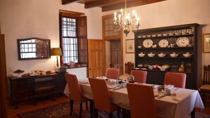 A dining room with a wooden table set for six, surrounded by chairs. A chandelier hangs from the ceiling, and a china cabinet is visible in the background. - Cape Dutch at Keerweder (Franschhoek)
