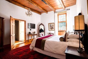A bedroom with a bed, a television, a mirror, a window, and a chandelier. - Cape Dutch at Keerweder (Franschhoek)
