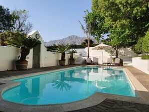 A swimming pool with lounge chairs and potted plants, surrounded by a white wall and a mountain view. - Cape Dutch at Keerweder (Franschhoek)