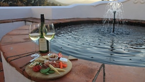 A dining table with a bottle of wine, glasses, and a variety of snacks and cheeses. - Cape Dutch at Keerweder (Franschhoek)