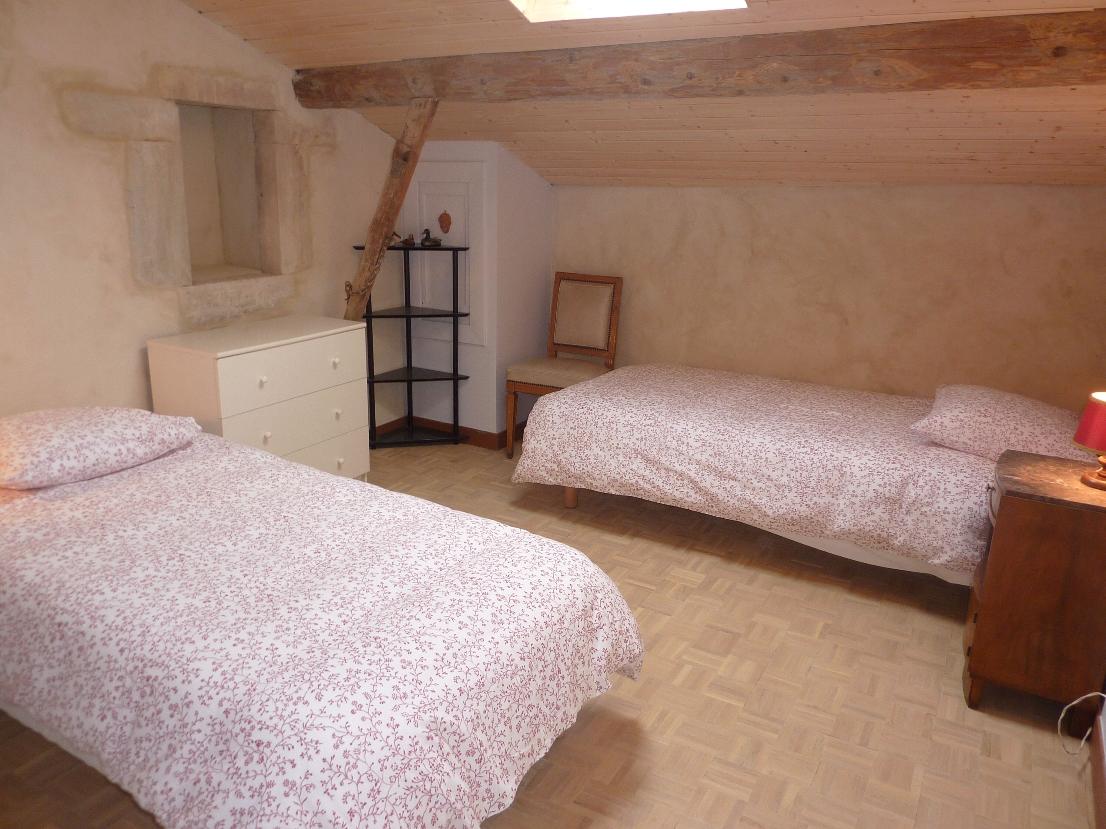 A bedroom with two beds, a wooden dresser, a small table, and a chair.