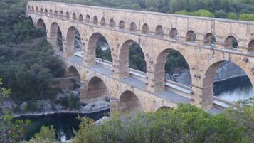 A stone aqueduct with multiple arches spanning a river, surrounded by dense greenery.