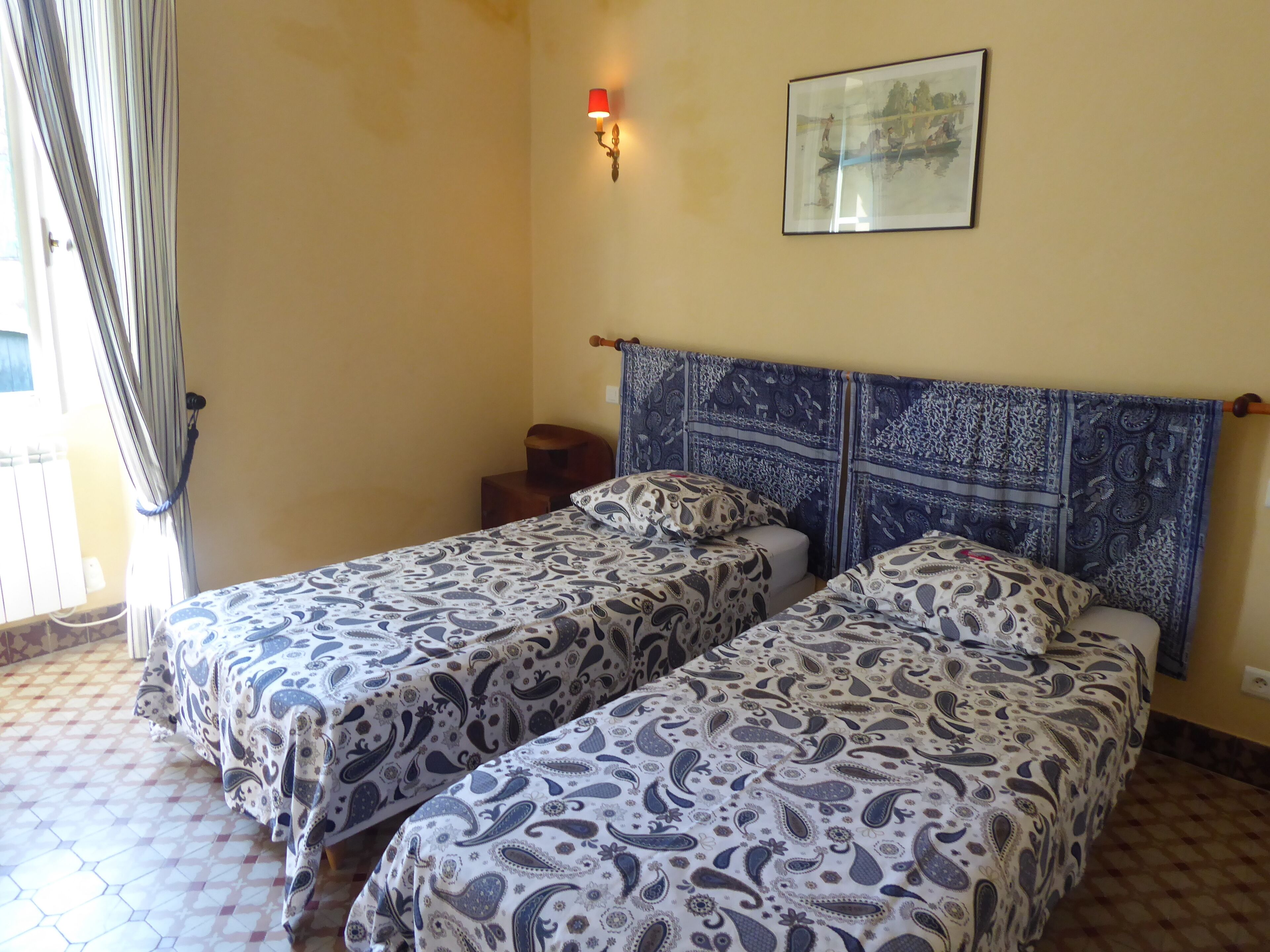 Una habitación con dos camas, una mesita pequeña, una lámpara de pared y un cuadro enmarcado.