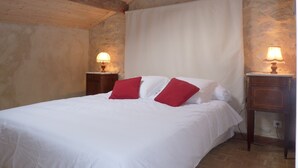 Un dormitorio con techo de madera, paredes de piedra, cama con ropa de cama blanca y almohadas rojas, y lámparas de noche.