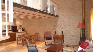 Amplia sala de estar con una mesa de comedor y sillas, una mesa de centro de madera, chimenea y cocina al fondo.