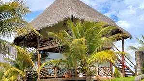 A thatched-roof structure with a wooden deck, surrounded by palm trees and a well-maintained lawn. - Pousada Theodora (Luis Correia)