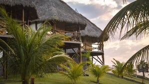 A resort with thatched-roof buildings, palm trees, and a grassy area. - Pousada Theodora (Luis Correia)