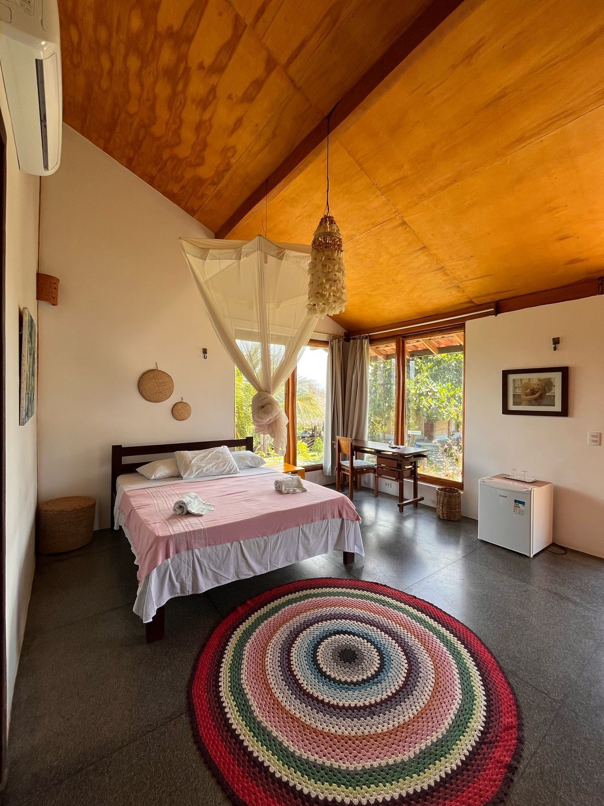 A bedroom with a bed, bedside table, chair, desk, and a small refrigerator.