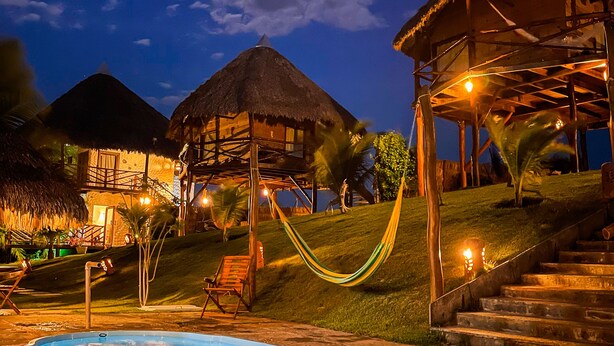 A pool area with a hammock, thatched-roof structures, and a staircase leading to a covered area. - Pousada Theodora (Luis Correia)