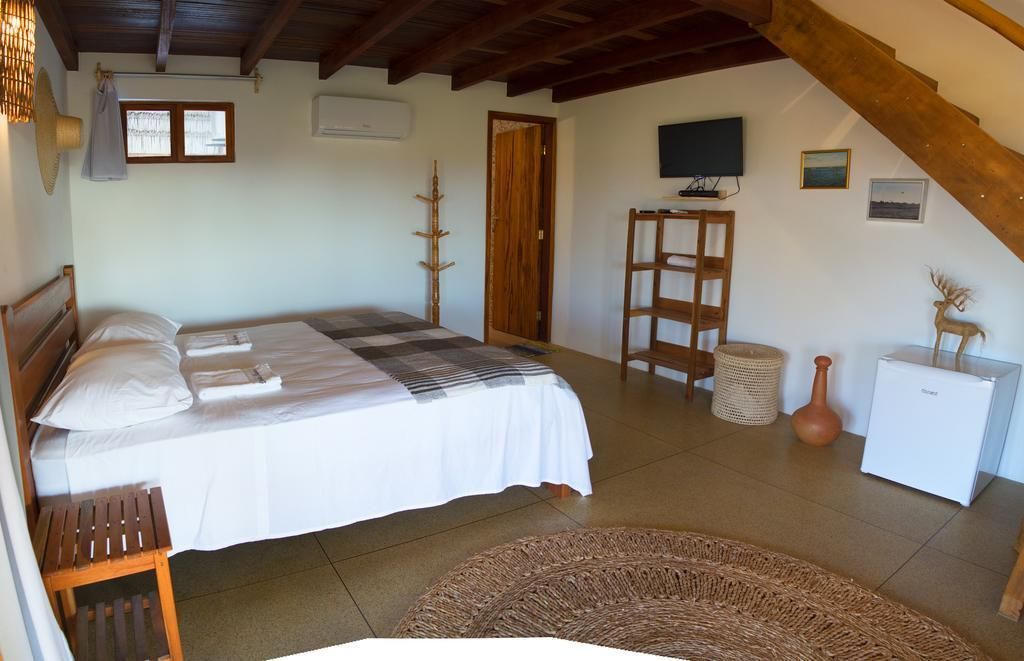 Un dormitorio con cama, una silla de madera, una mesita, un tapete tejido y un televisor en la pared.